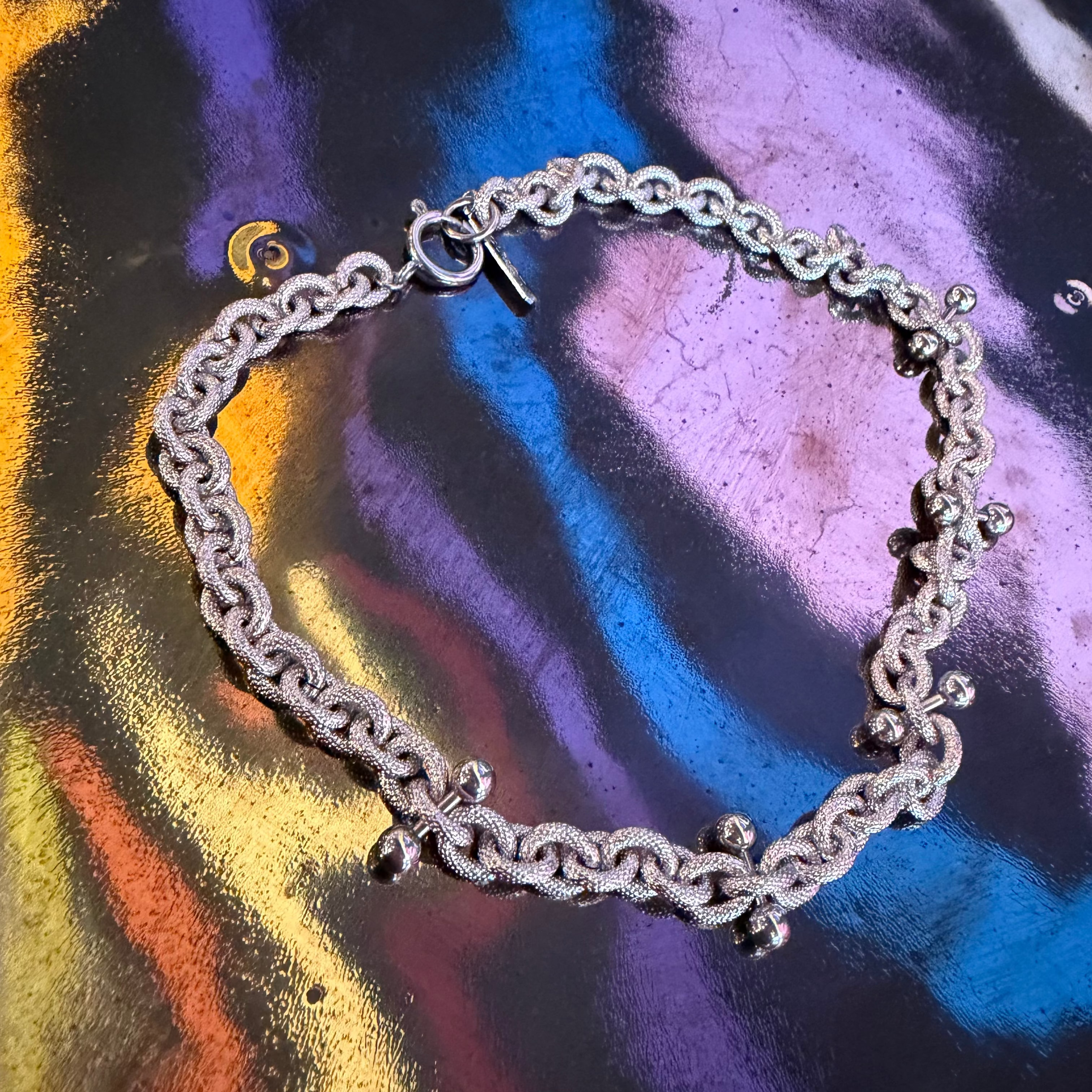 Silver chain necklace on a colorful, reflective surface